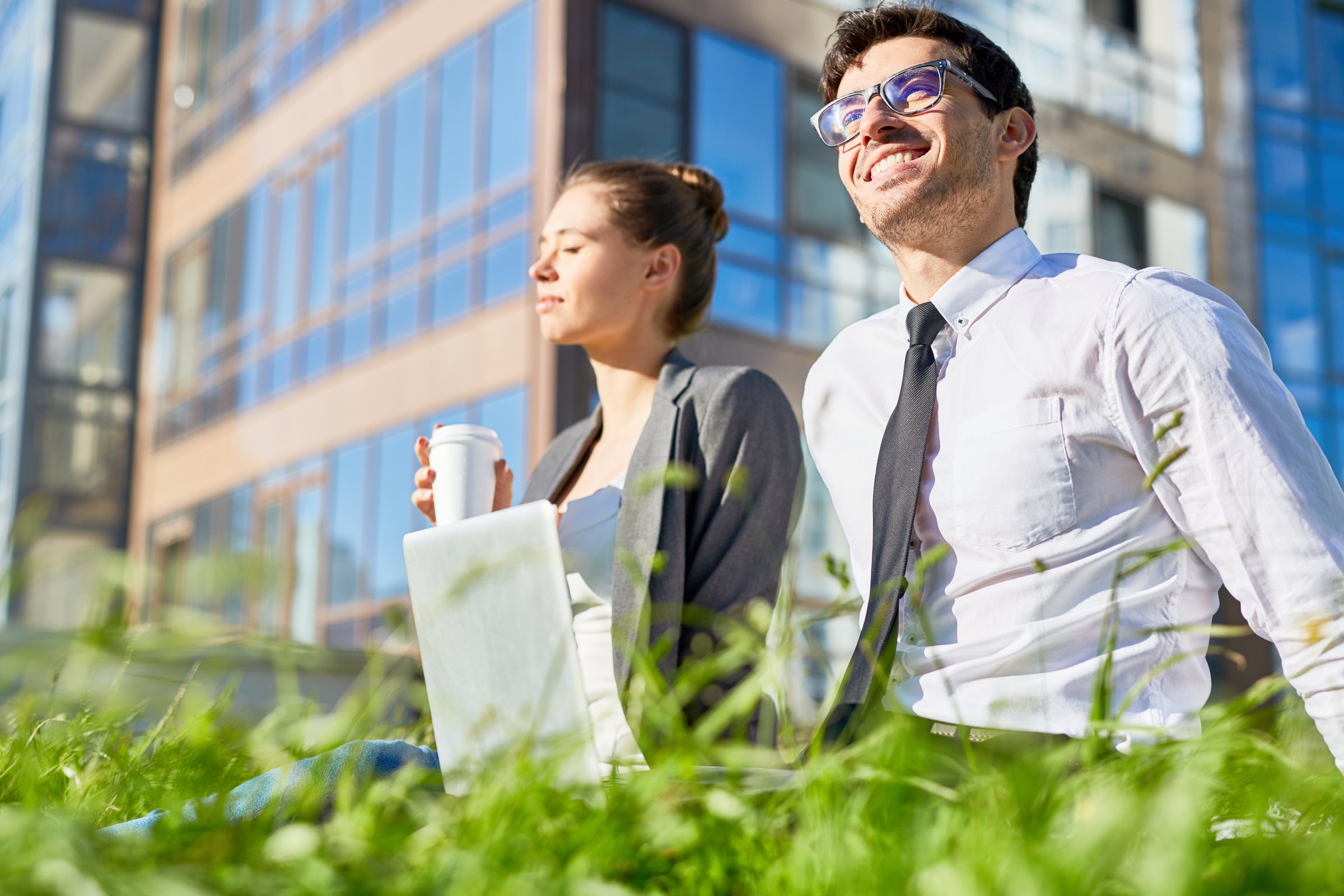 Una donna con un bicchiere di caffè e un uomo in camicia sorridono all'aperto davanti a un edificio a vetri