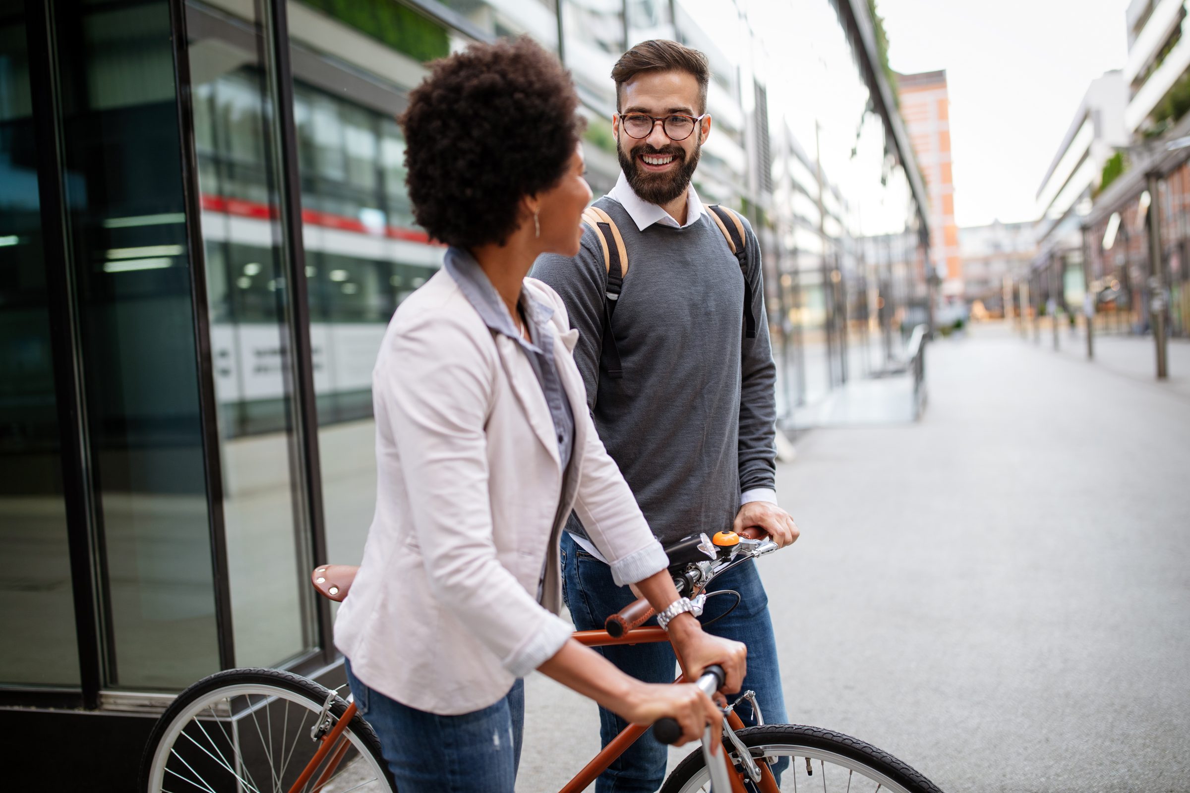 Due persone sorridono per strada, una porta la bicicletta a mano